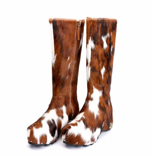 Luxury handmade knee-high platform boots crafted from genuine calf hair with a brown and white natural hide pattern. Features round toe, side gold zipper, and studded sole accents. Unique statement footwear for bold, high-end fashion looks.