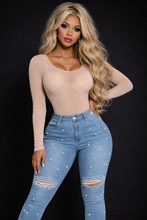 Woman wearing a beige long-sleeve top and blue jeans with embellishments on a black background

bellarosecouture.com

