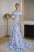 Woman in a light blue off-shoulder gown with floral details in an elegant room.

The La Roseraie Gown is an exquisite expression of modern couture and timeless femininity. Designed to sculpt and flatter, this off-the-shoulder mermaid silhouette elegantly frames the neckline while contouring the waist and hips for a refined, elongated look.

Crafted with a structured bodice and smooth, body-skimming fabrication, the gown flows effortlessly into a dramatic floor-length train adorned with hand-placed three-dim