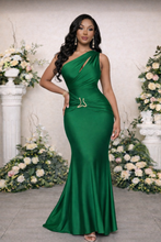 Woman in a green evening gown standing in front of floral decorations.
Luxury emerald green one-shoulder satin gown featuring a sculpted silhouette, ruched waist detailing, and signature gold serpent clasp, designed for elegant evening wear and formal occasions.